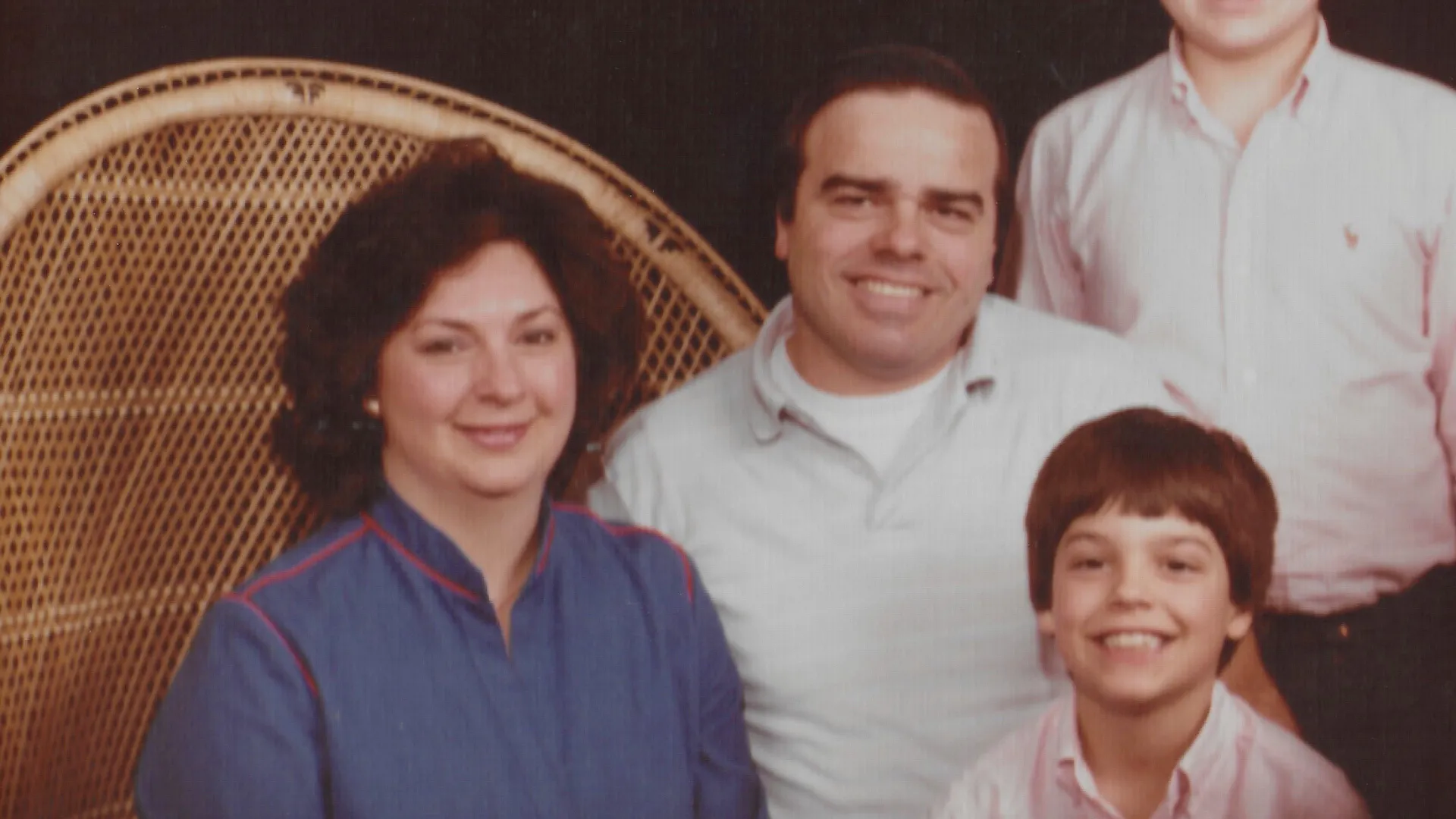 Picture Of 4 people, 3 of which are sitting on a wicker basket chair, 1 standing with head cut off during image cropping